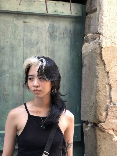 Artist Isip Xin stands next to a wooden door wearing a black tank top.